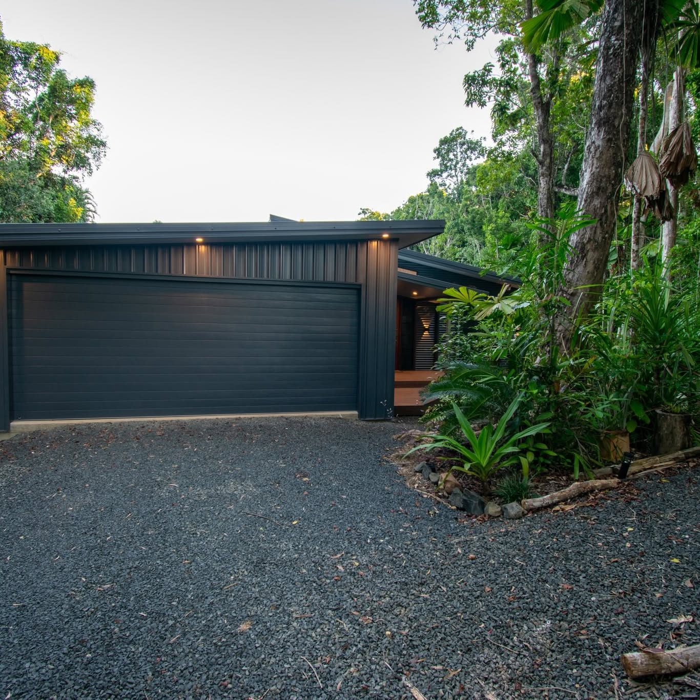 The front of the home at dusk with the eave lights on and rainforest either side