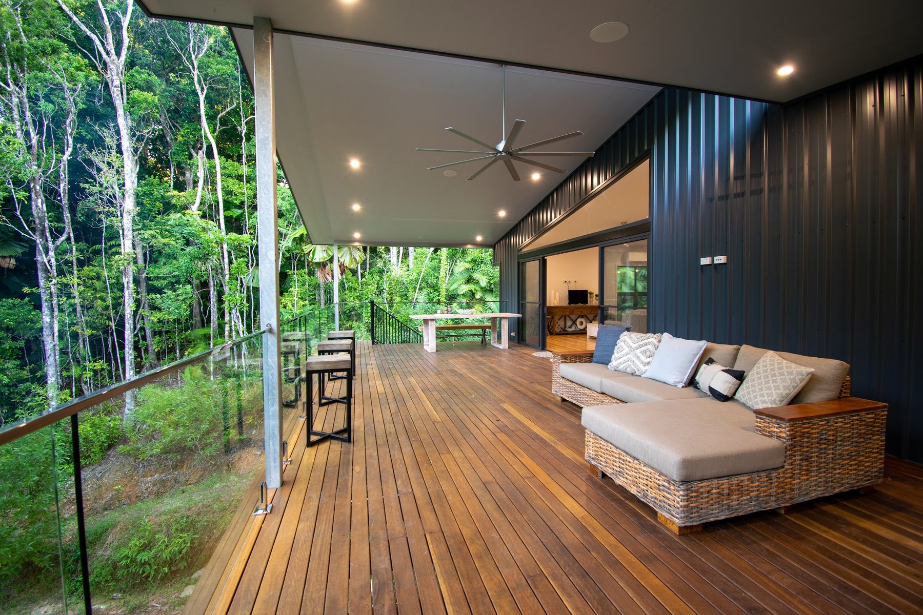 The covered deck of the rainforest home, a large ceiling fan overhead and downlights through the soffit